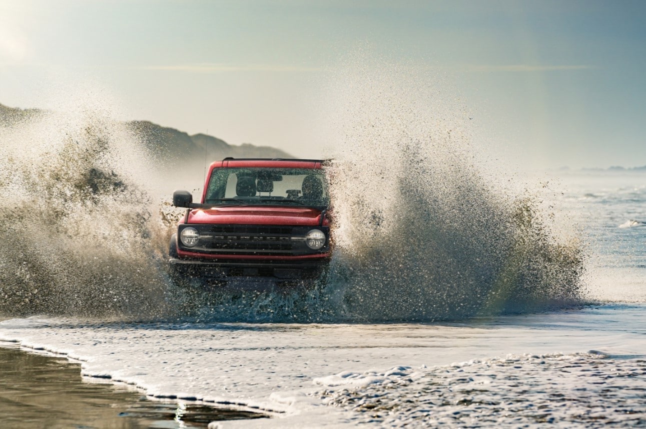 a red 2021 Ford Bronco driving in water and splashing high