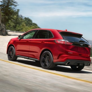 A
red 2019 Ford Edge driving on a curvy road with a green forest on the left
overlooking a bay of water on the right