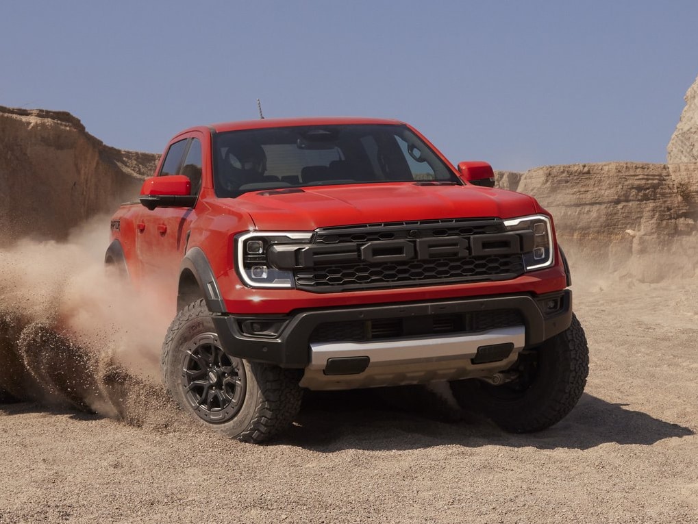 A Red 2023 Ford Ranger Raptor Driving in a dessert, kicking up sand with it's wheels mid-turn