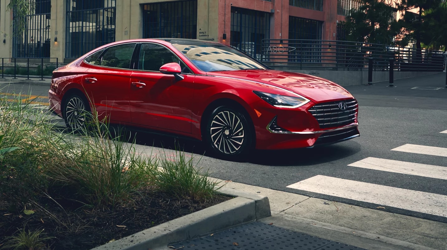 A red 2023 Hyundai Sonata in profile view as it sits at a city intersection