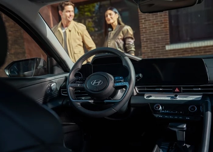 Couple walking up to a 2026 Hyundai Elantra Hybrid, seen from the driver's seat, with proximity key entry