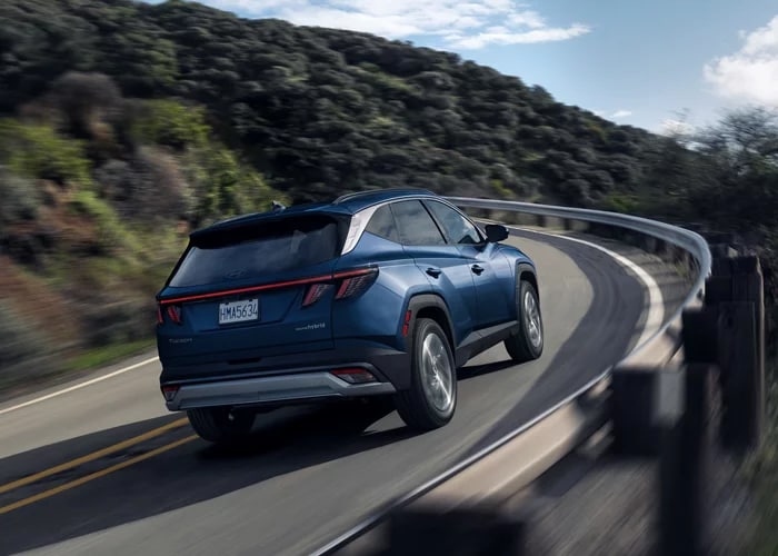 Blue 2026 Hyundai Tucson Hybrid with HTRAC AWD driving a winding mountain road, rear three-quarter view