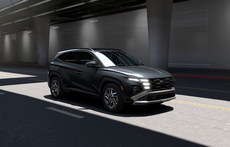 Front three-quarter view of a dark gray 2026 Hyundai Tucson Hybrid compact SUV parked in an urban underpass
