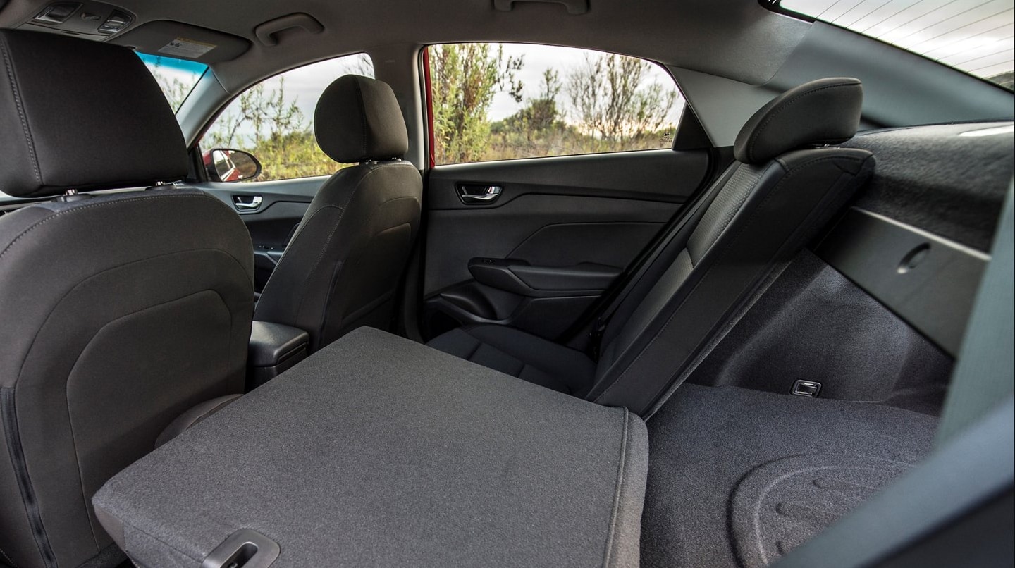 A view of the interior cabin of a 2022 Hyundai Accent upholstered in a dark gray with the rear seat folded down revealing storage space in the trunk