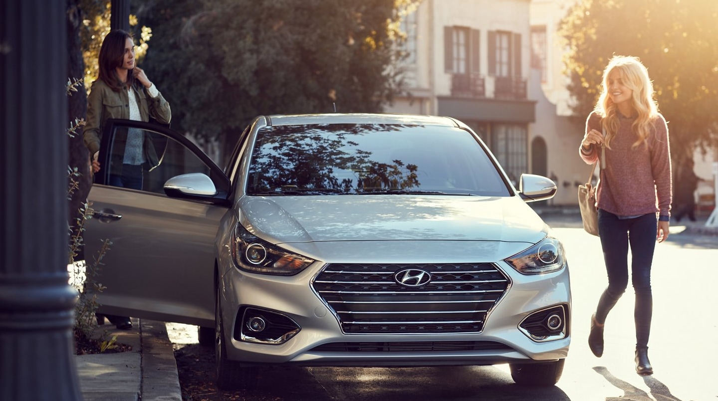 A view of the front and grille of a silver 2022 Hyundai Accent that sits parked on a city street