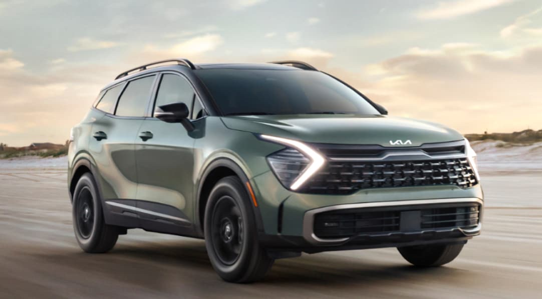 A gray-green 2023 Kia Sportage with headlights on driving down a country road