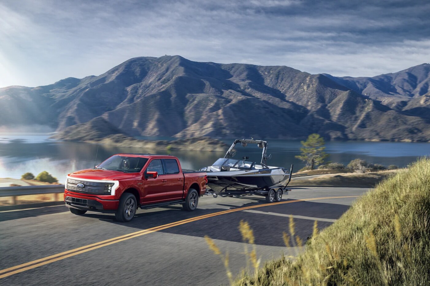 A red 2023 Ford F-150 hauls a speedboat down a country highway