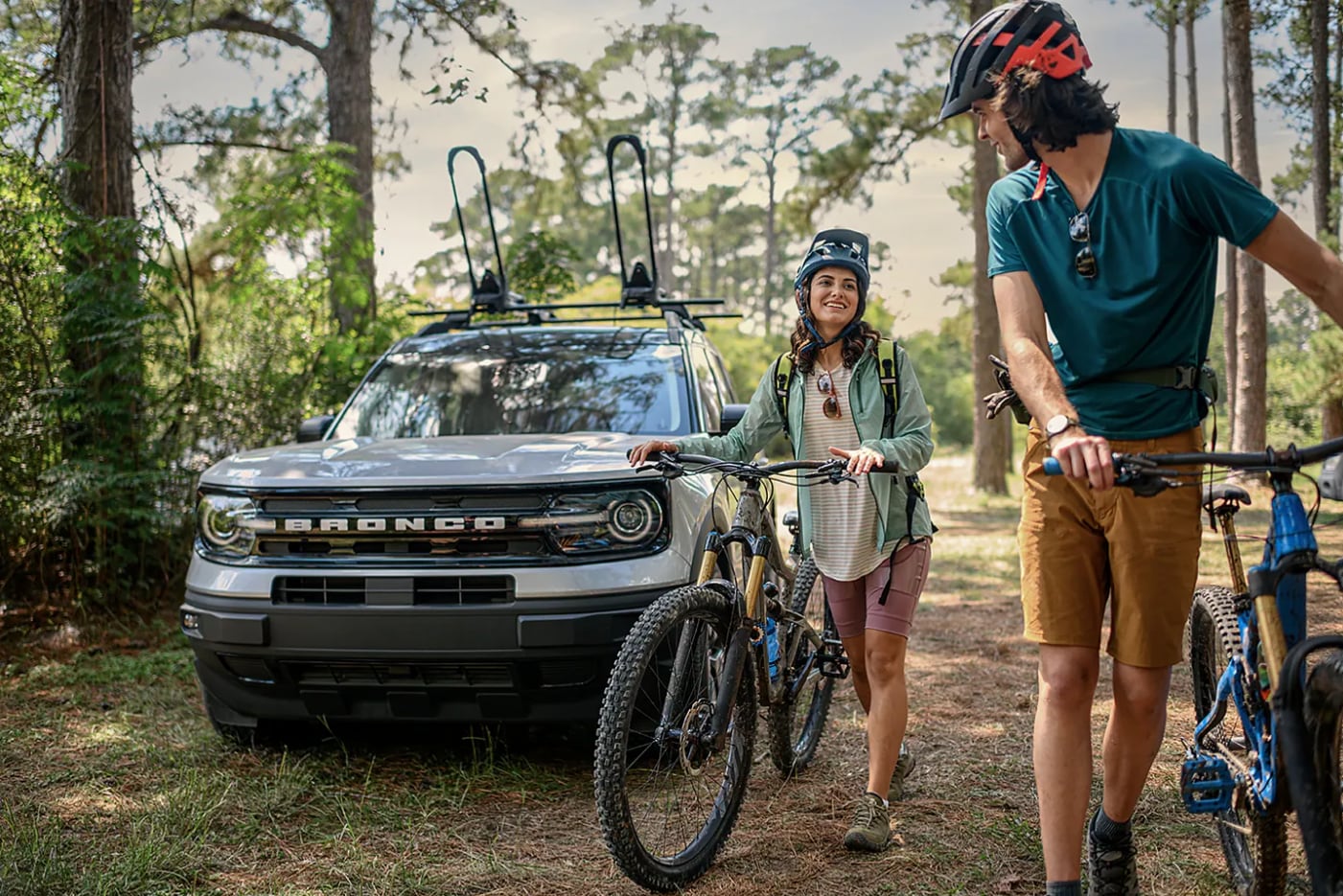 A gray 2023 Ford Bronco Sport Outer Banks Edition sits parked while a couple walk in front of it with mountain bikes