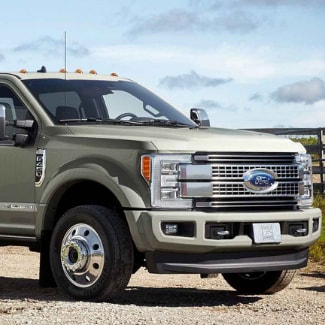 The front side of a light gold 2019 Ford Super Duty parked outside the
fence of a farm after pulling a heavy load with green grass and blue skies in
the background