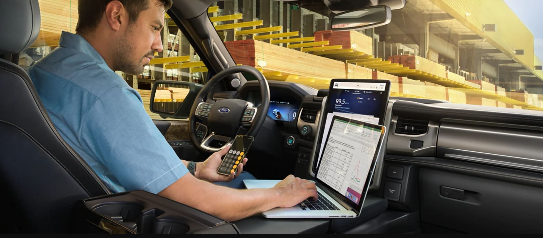 A man sits in the driver's seat and uses the large center console of the Ford F150 Lightning's cabin as a work surface for his laptop
