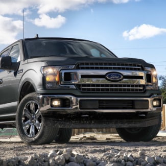 A close up view from the ground of a black 2019 Ford f-150 parked in a
construction site with rocks in the foreground and a partly cloudy blue sky in
the background