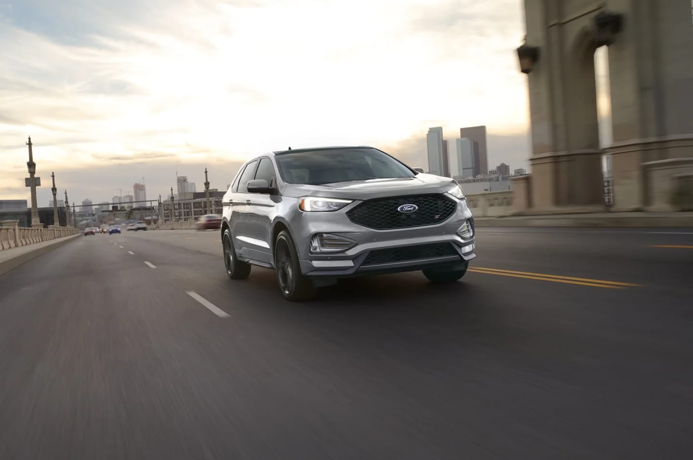 A gray 2024 Ford Edge drives toward the viewer on a city street