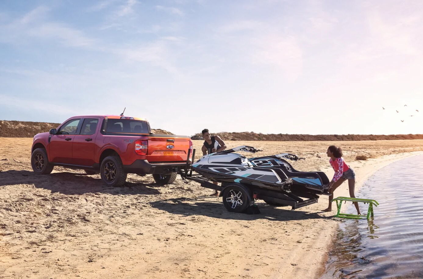 A red 2022 Ford Maverick unloading a jet ski at the beach.