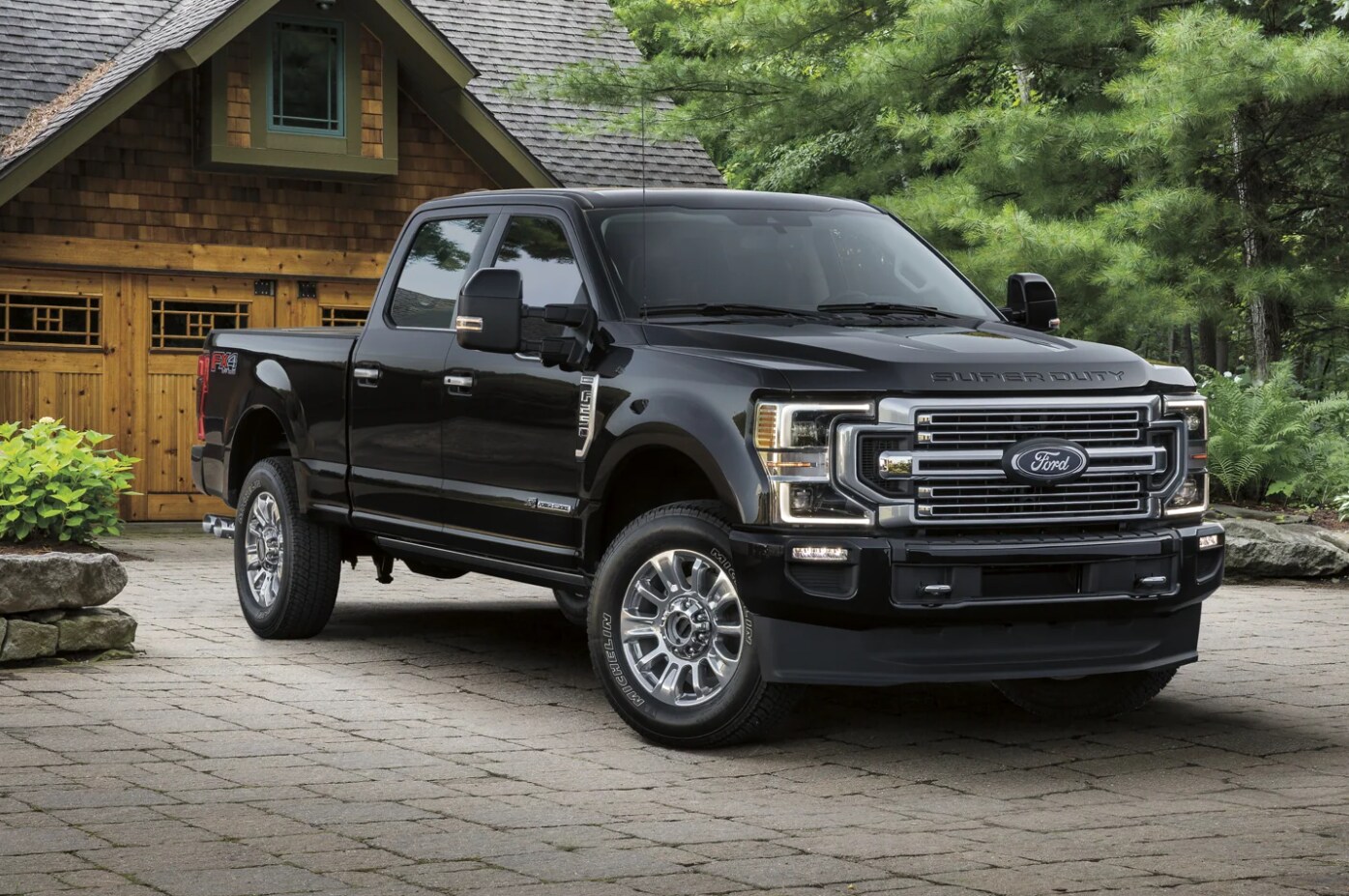 A black 2022 Ford Super Duty with dark tinted windows and alloy rims sits parked on a brick driveway in front of a craftsman style garage on a sunny day, showing the front chrome grille and angled profile