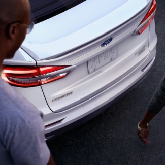 A birds eye view of two people walking by and admiring the back of a
white 2019 Ford Fusion