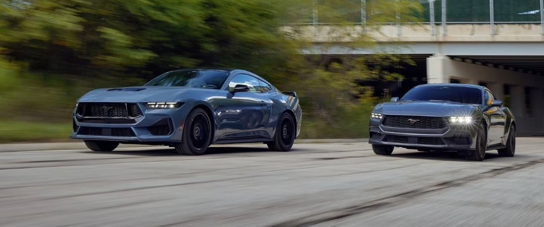 Two new black 2024 Ford Mustangs driving down a highway.