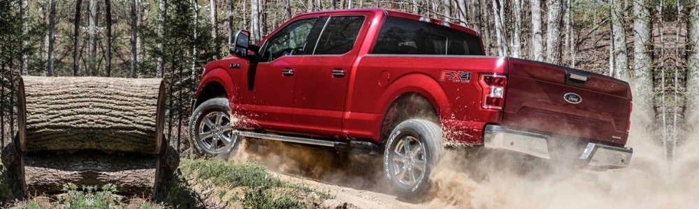 Driver side view of a red 2019 Ford F-150 truck sliding through dirt around a curve through a thick forest