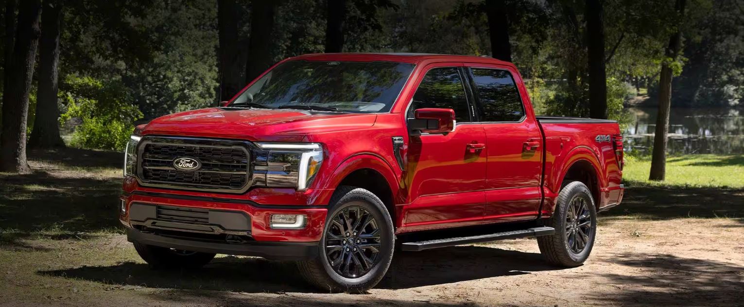 A red Ford F-150 parked in front of a lake surrounded by forest.