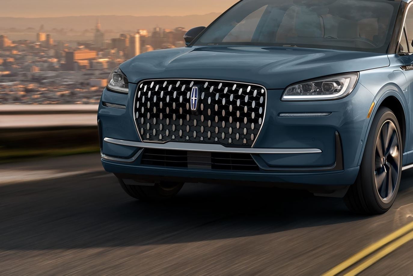 A blue Lincoln Corsair driving up a mountain pass overlooking a city scape.