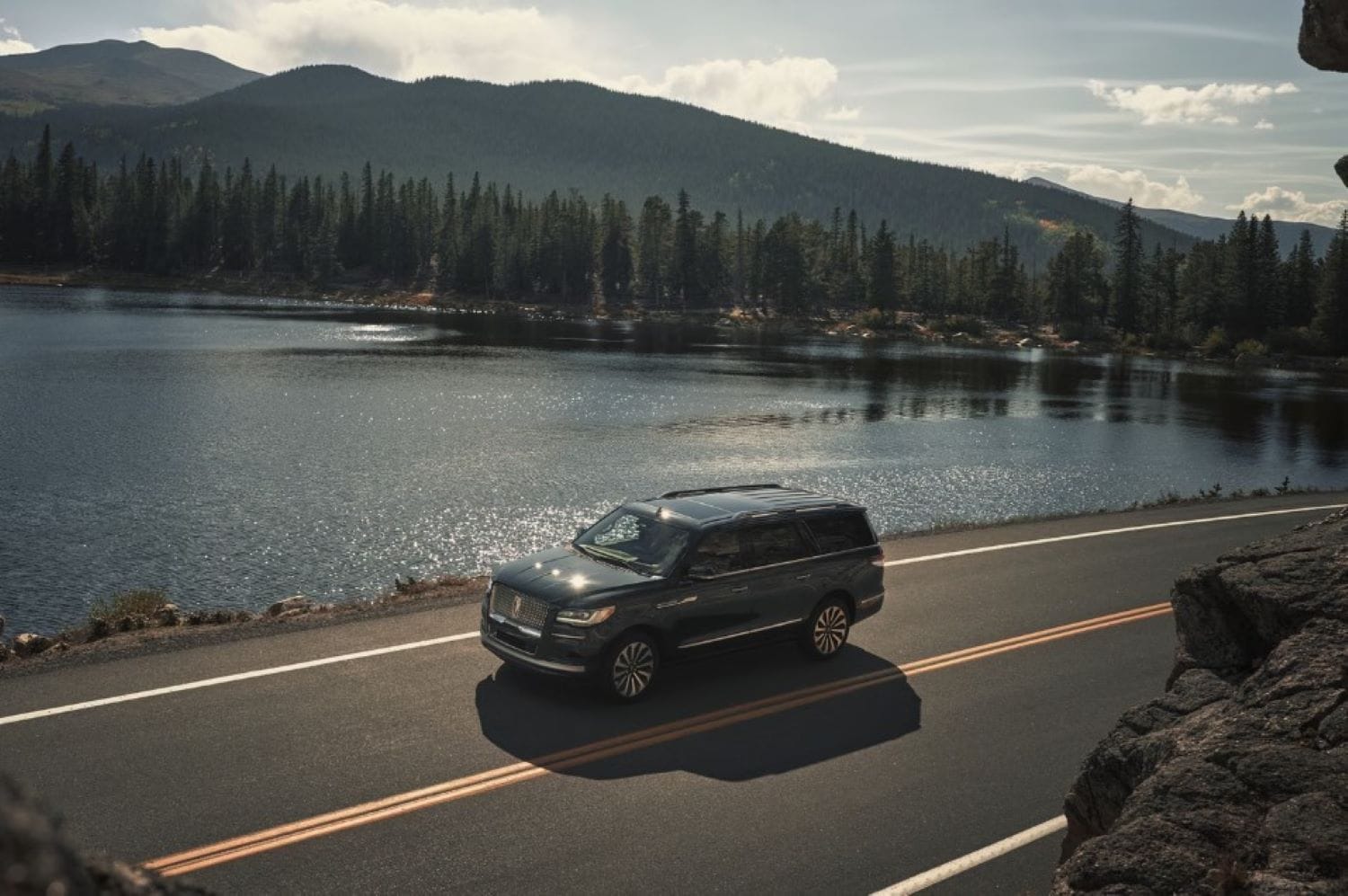 A Lincoln driving next to a mountain lake.