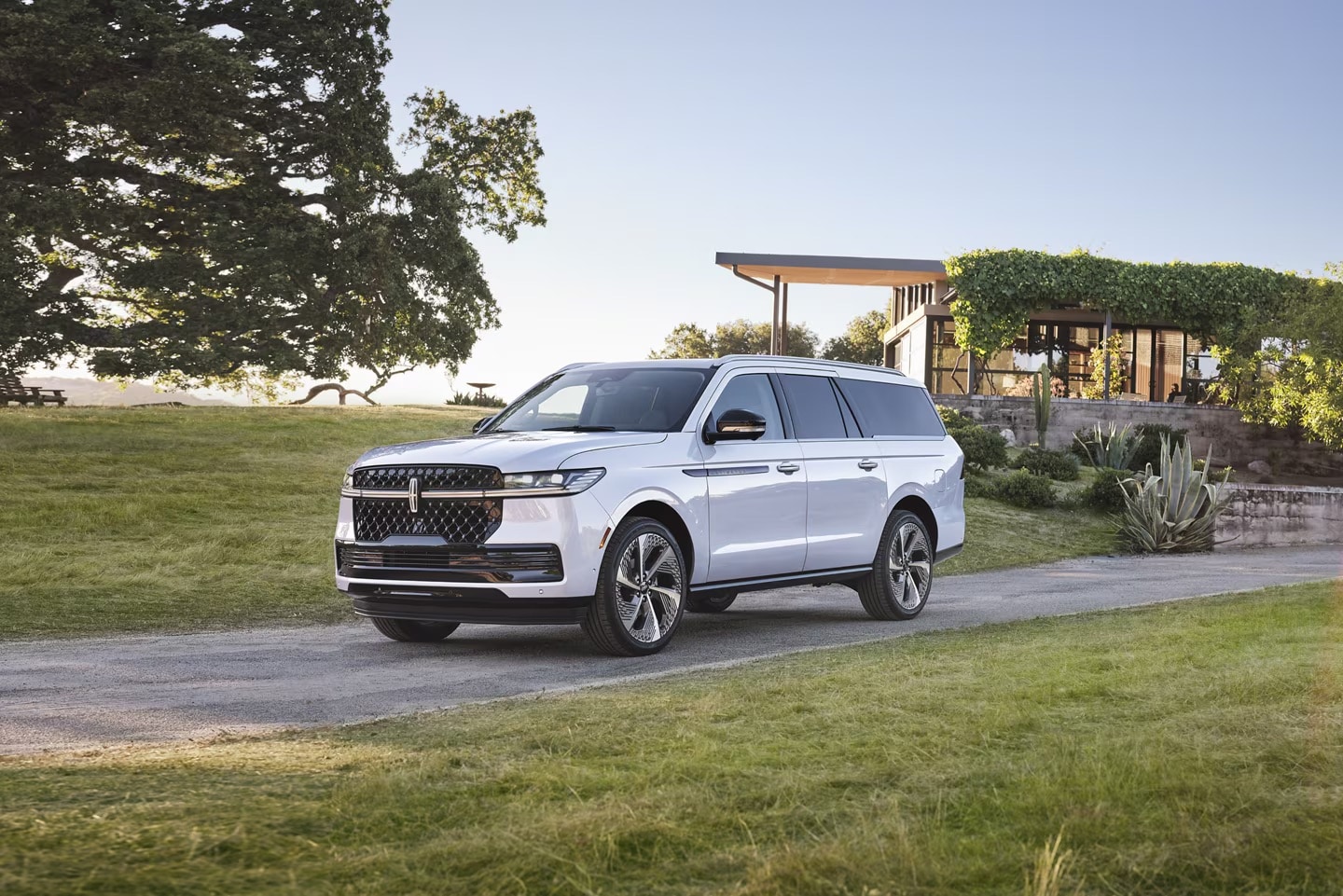 A white Lincoln Navigator driving down a long driveway.