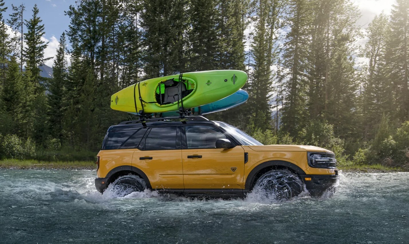 All new Ford Bronco Sport splashing in deep water with a kayak loaded on the top rack