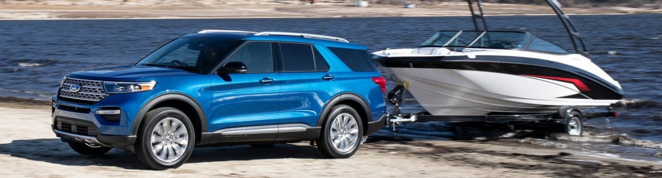 Exterior side view of a 2020 Ford Explorer towing a large boat out of a lake