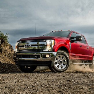 A red 2019 Ford Super Duty turning around the curve of a dirt path with
dust flying from the tires under the truck on a partly cloudy day