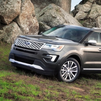 A dark silver 2019 Ford Explorer driving up a grassy hill around some
big rocky boulders sitting in the background