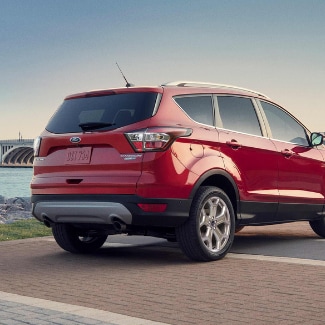 The back right side of a red 2019 Ford Escape parked on a brick platform
overlooking a rocky shore beside a river that runs under a bridge in the
distance