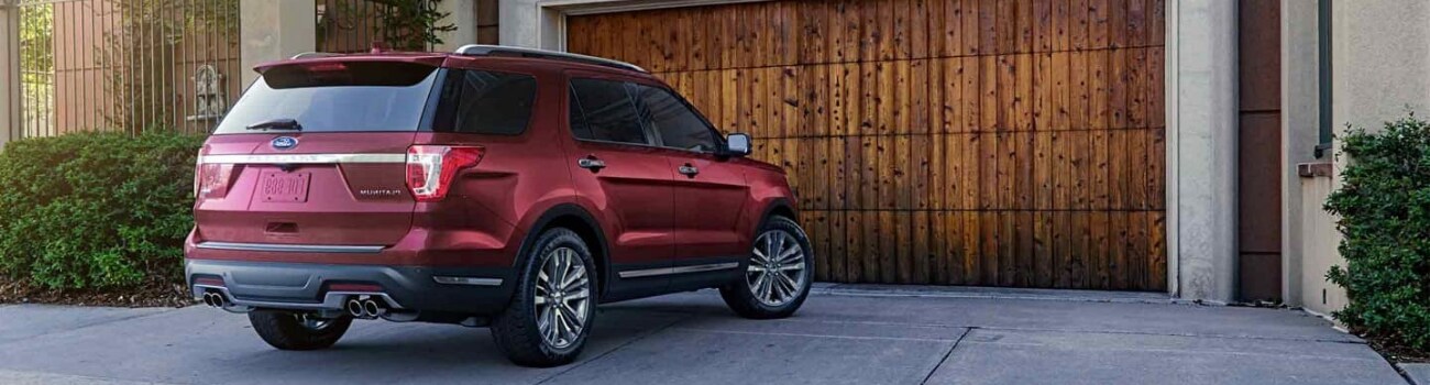 Back passenger side view of a red 2019 Ford Explorer parked in a driveway in front of a wooden slated garage door