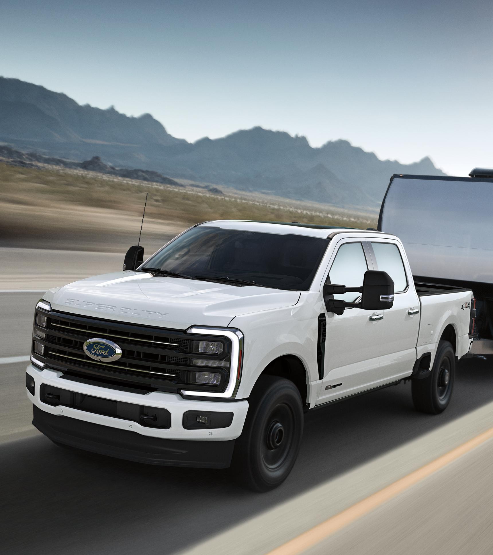 White Ford truck pulling a large fifth-wheel RV trailer down a scenic road