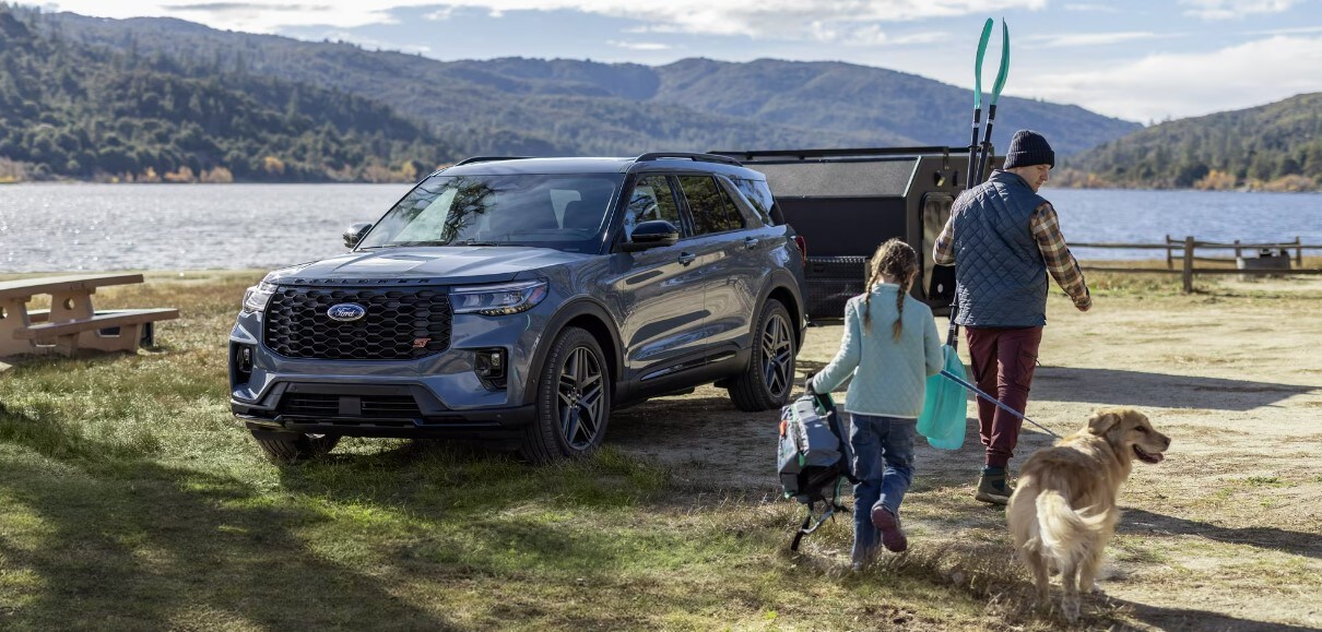 A grey 2025 Ford Explorer sits parked with a camper hitched on and a family walking back to the car.