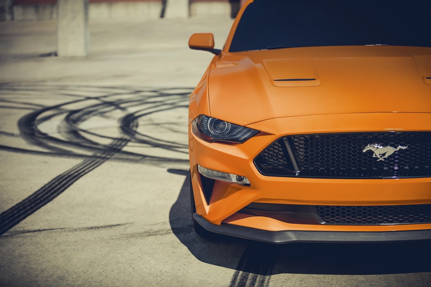 an orange 2020 Ford Mustang leaving tire marks on the pavement doing burn outs in a parking lot