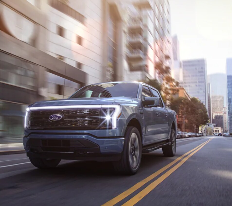 A bright blue F150 Lightning speeds through the city as the sun glints off the chrome on the front bumper