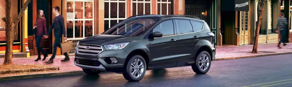 Driver side angle of a 2019 Ford Escape parked on a city side street in front of shops as blurred images of pedestrians walk by