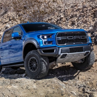 A blue 2019 Ford F-150 Raptor driving up a rocky cliff with a rocky
desert scenery in the background