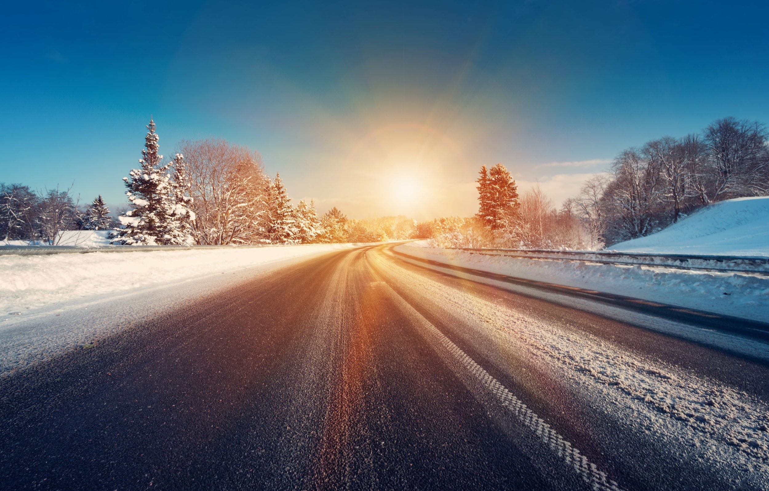 A snowy winter road with a forest surrounding it.