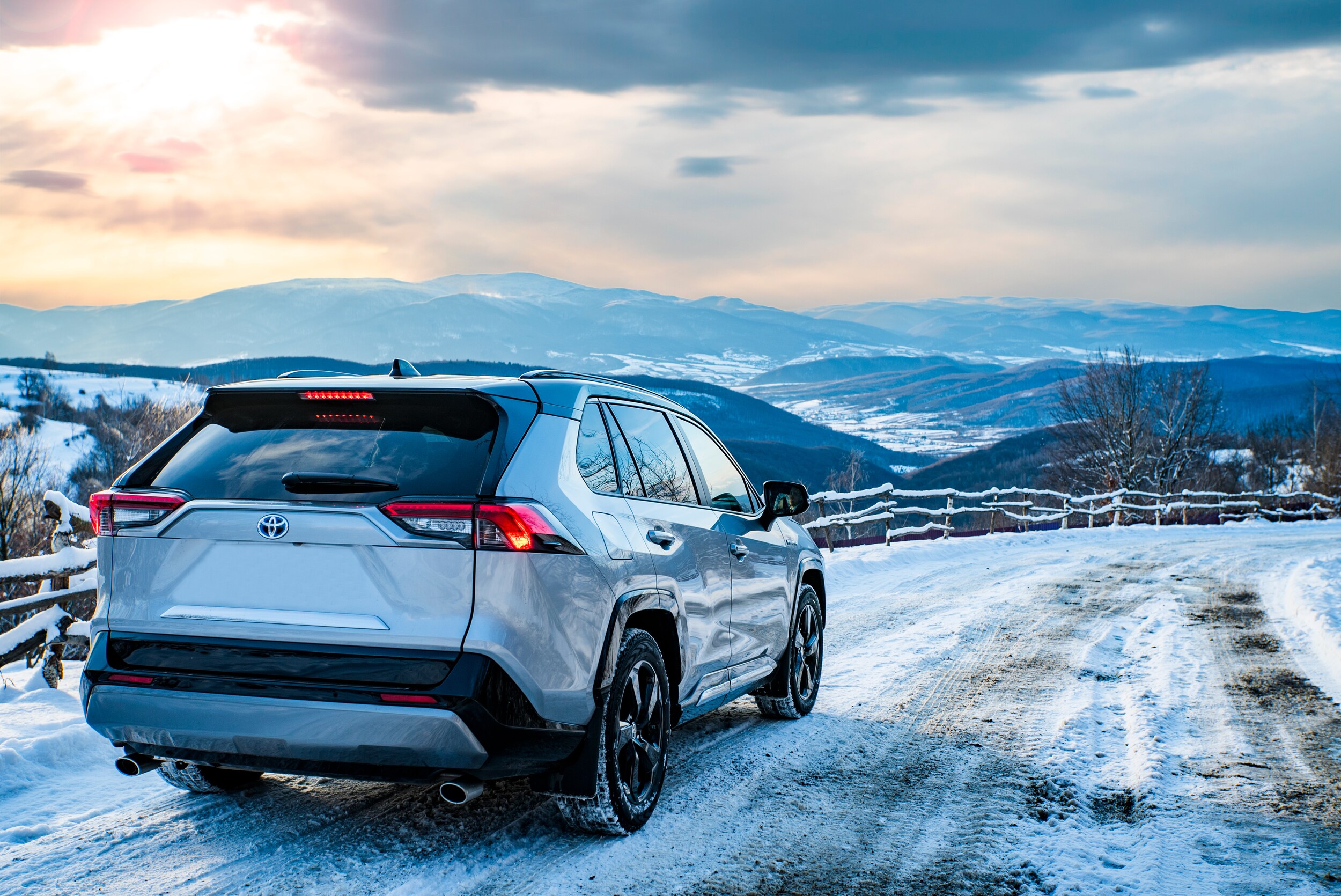 A Toyota Rav4 parked on a snowy mountain road at sunset. 