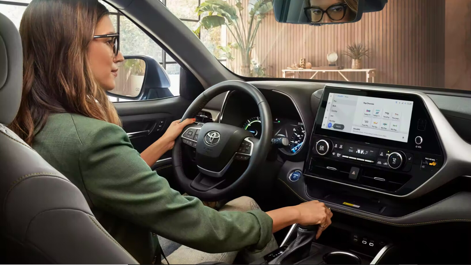 A woman driving a 2023 Toyota Highlander Hybrid and a view of the dash and infotainment system