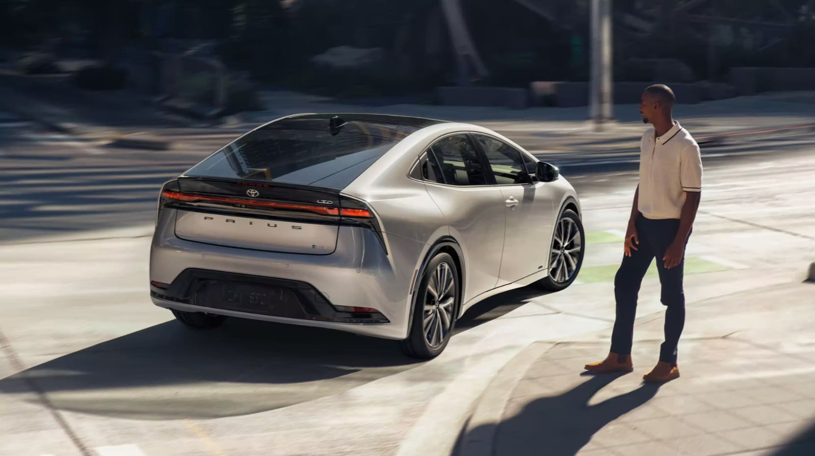 A view of the back of a silver 2023 Toyota Prius as it takes a right turn on a city street