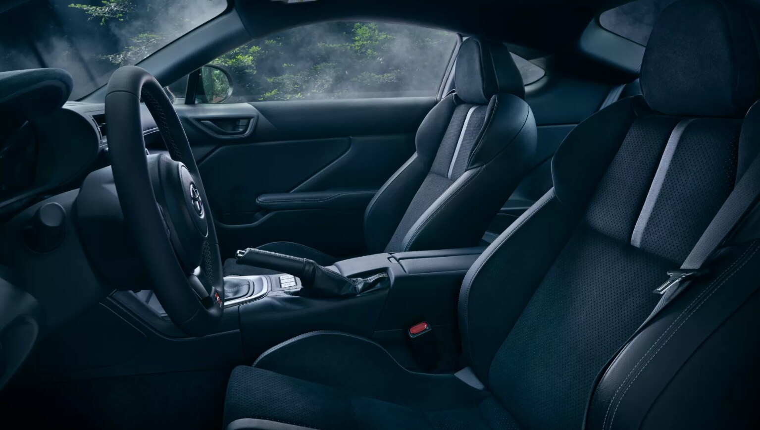 Looking in from the driver's side, a view of the Toyota GR86's all black interior is shown with two sporty front seats