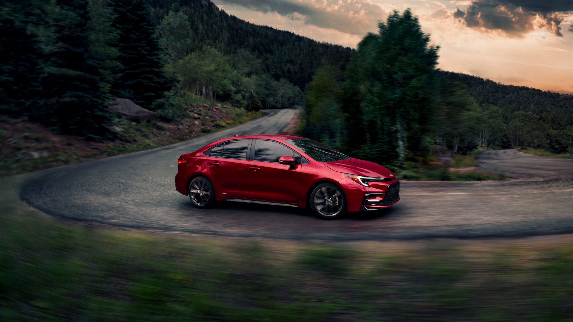 A red Corolla driving on a tight forest road.