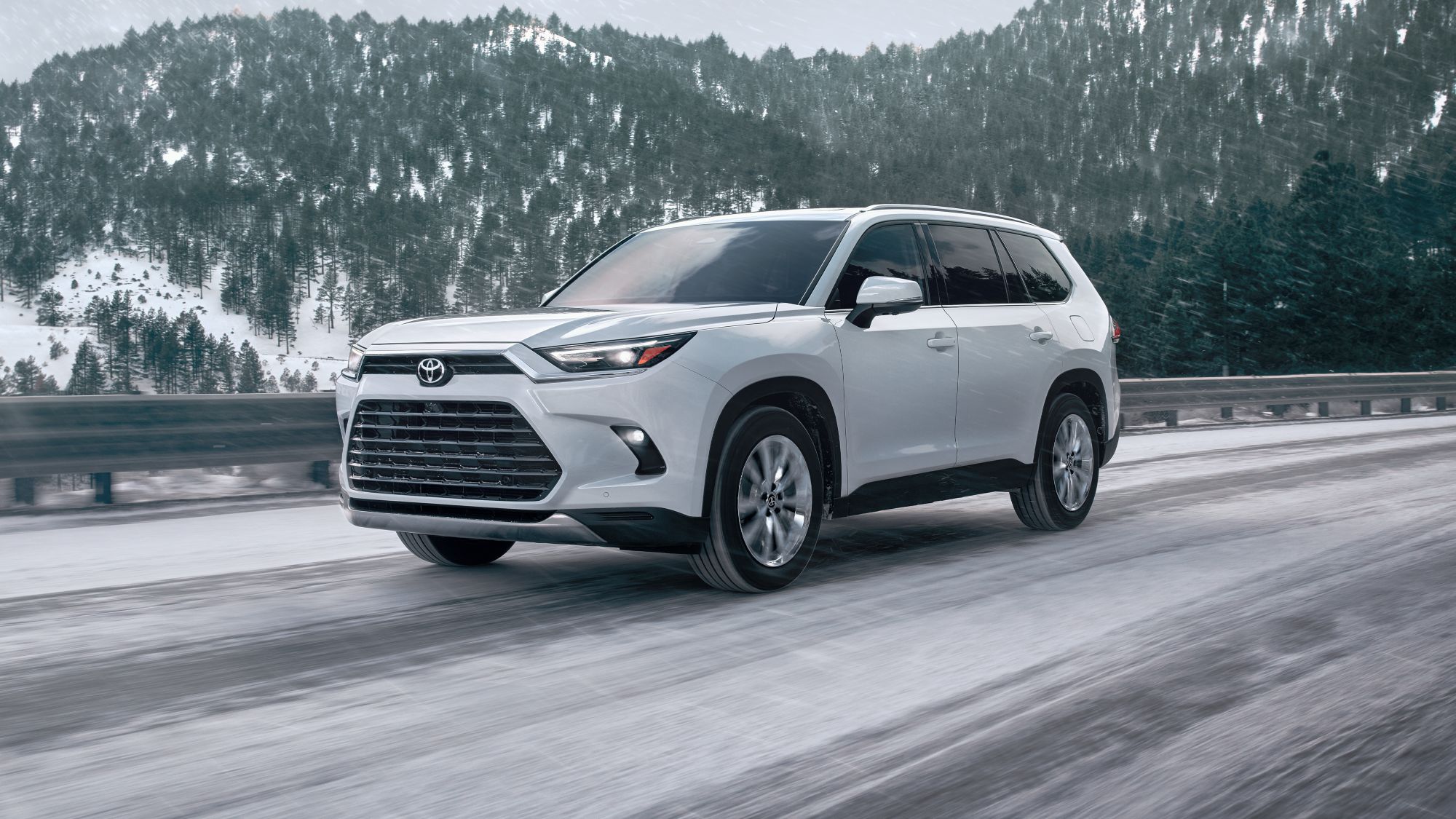 A white Grand Highlander driving through a snowy mountain pass.