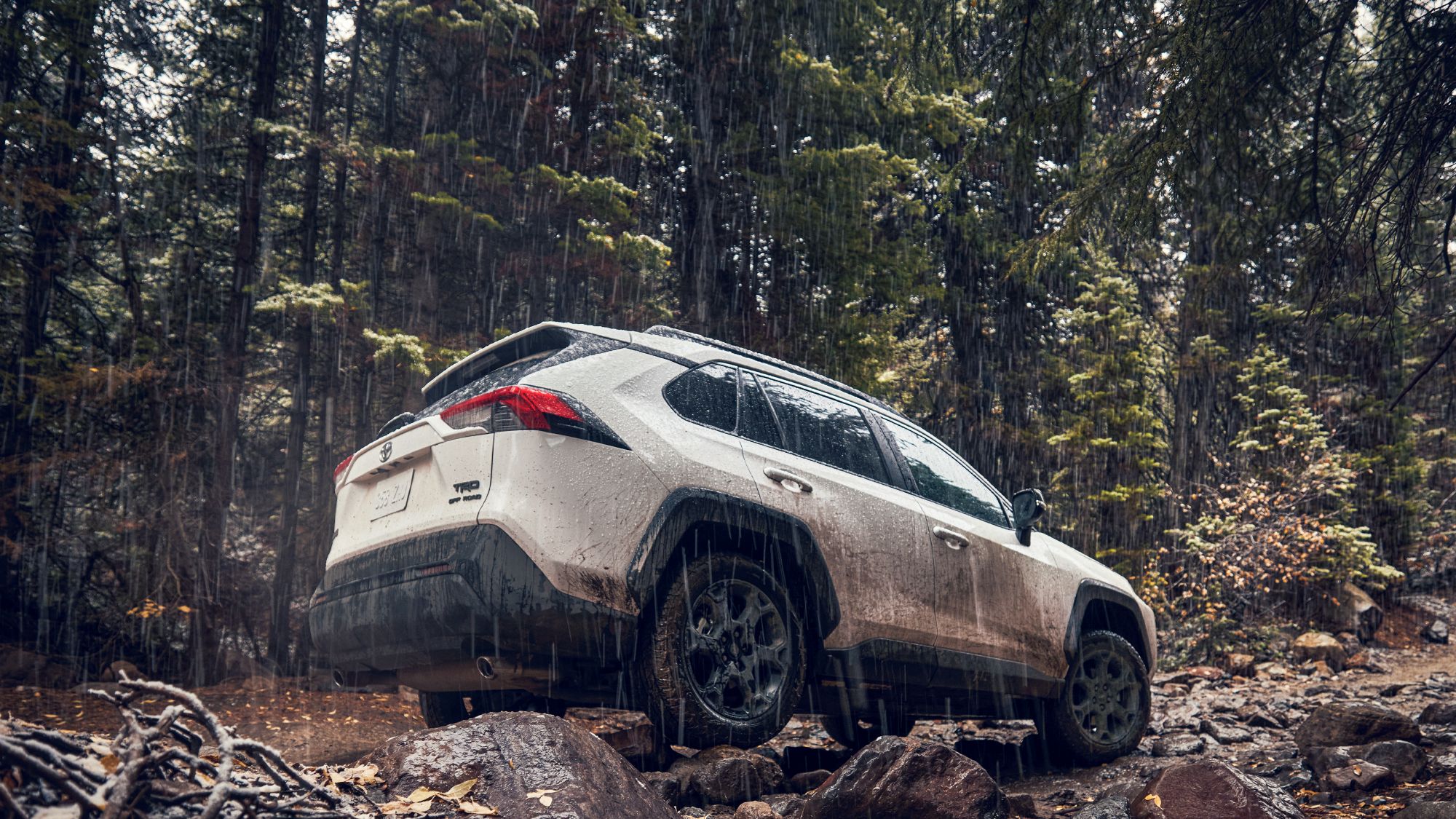 A white Rav4 driving over a rough dirt road in the rain.