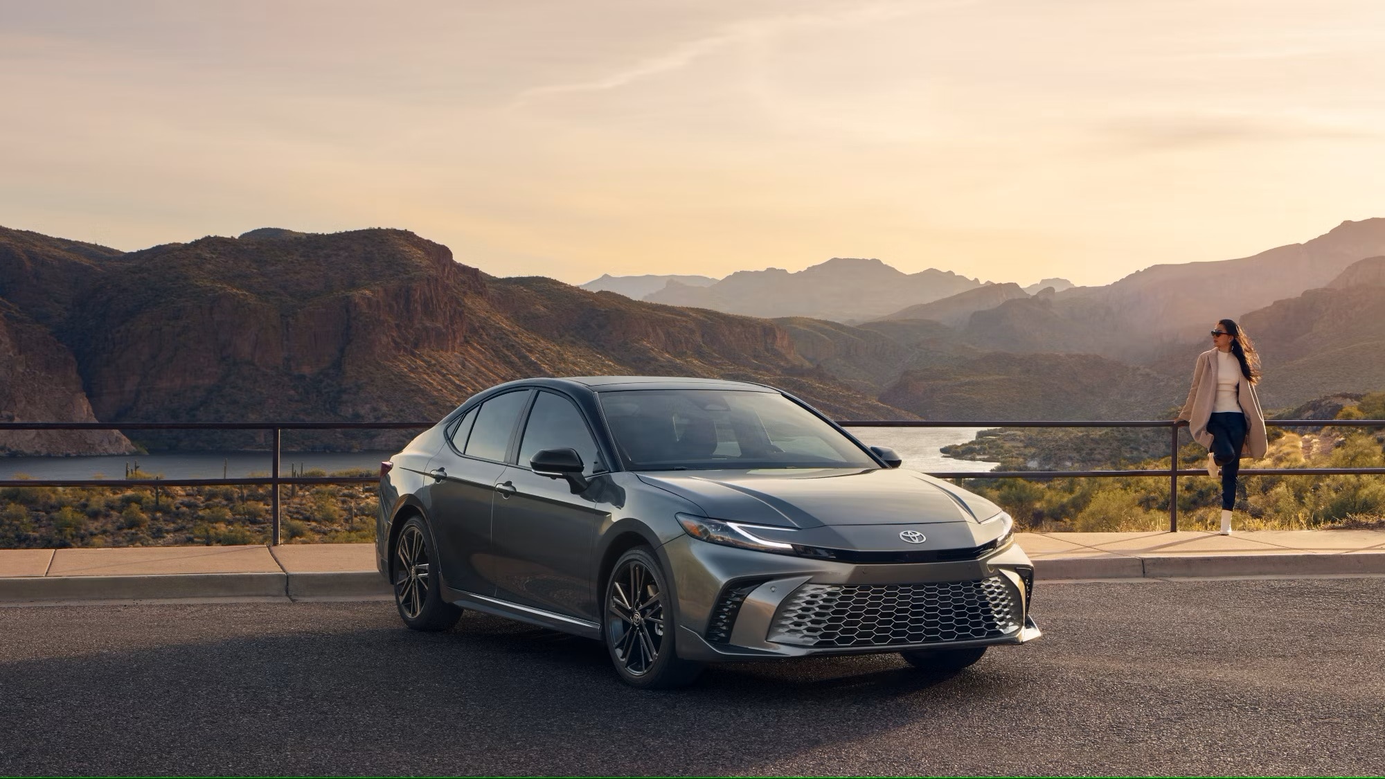 A 2025 Toyota Camry driving alongside a mountain road over a lake in a valley.