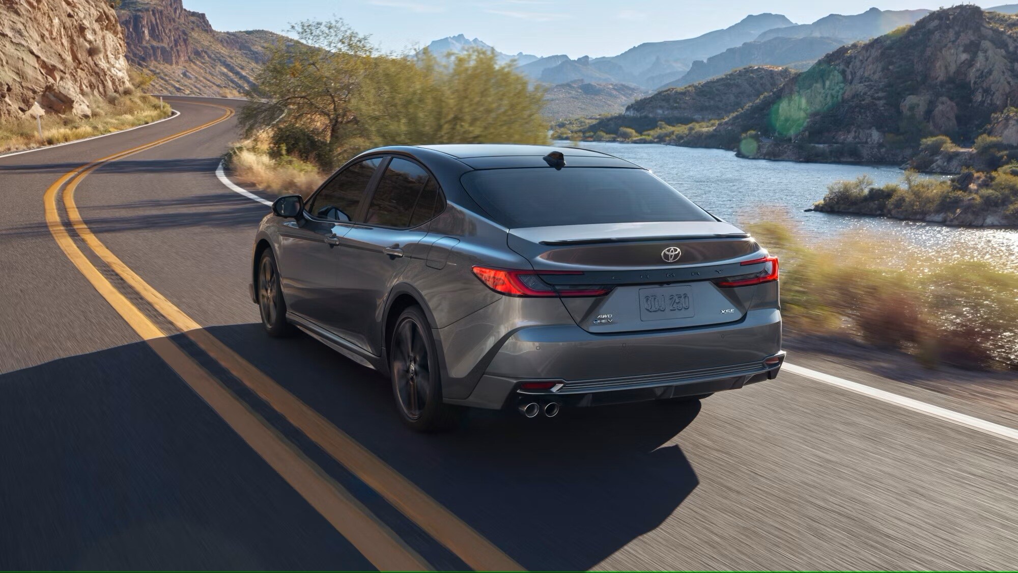 A 2025 Toyota Camry driving alongside a mountain road over a lake in a valley.