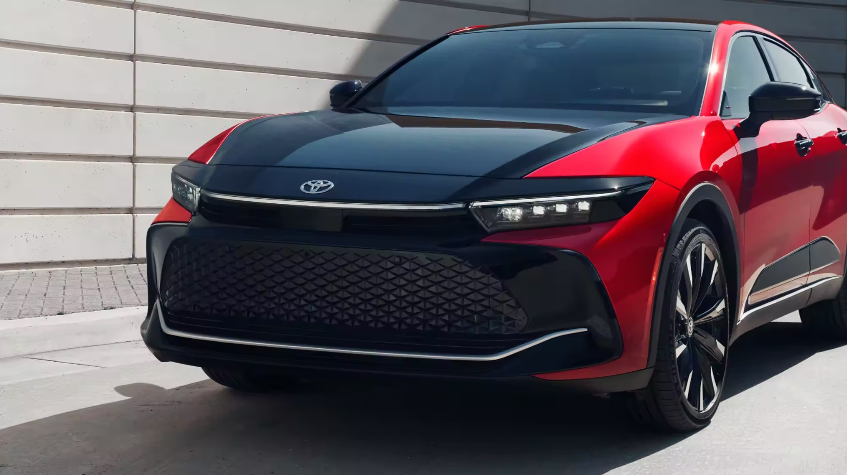 A close-up of the front and hood of a red and black 2023 Toyota Crown parked in the sun
