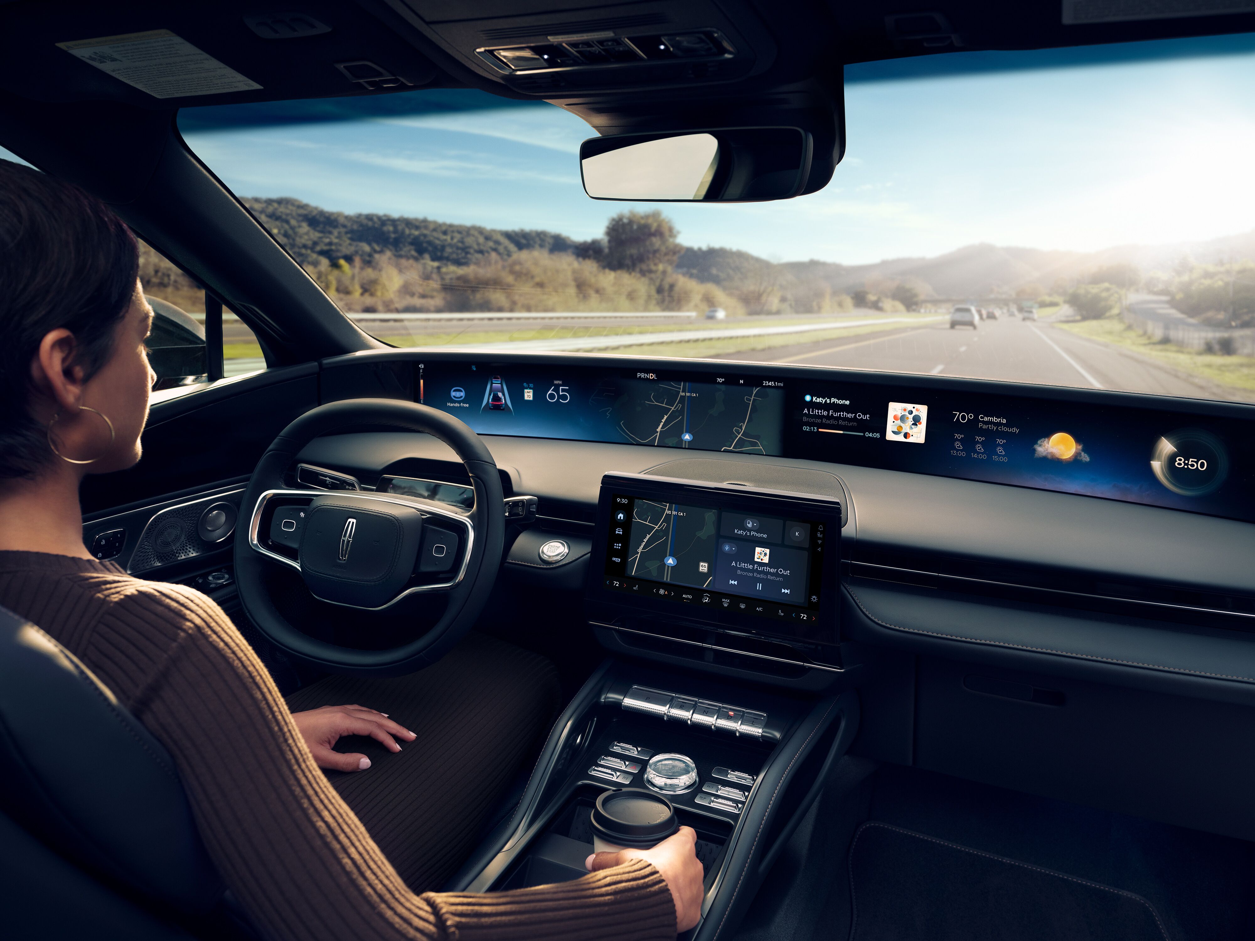 Driver behind the wheel of a 2027 Lincoln Nautilus showing the panoramic digital display and center touchscreen while driving on a highway.