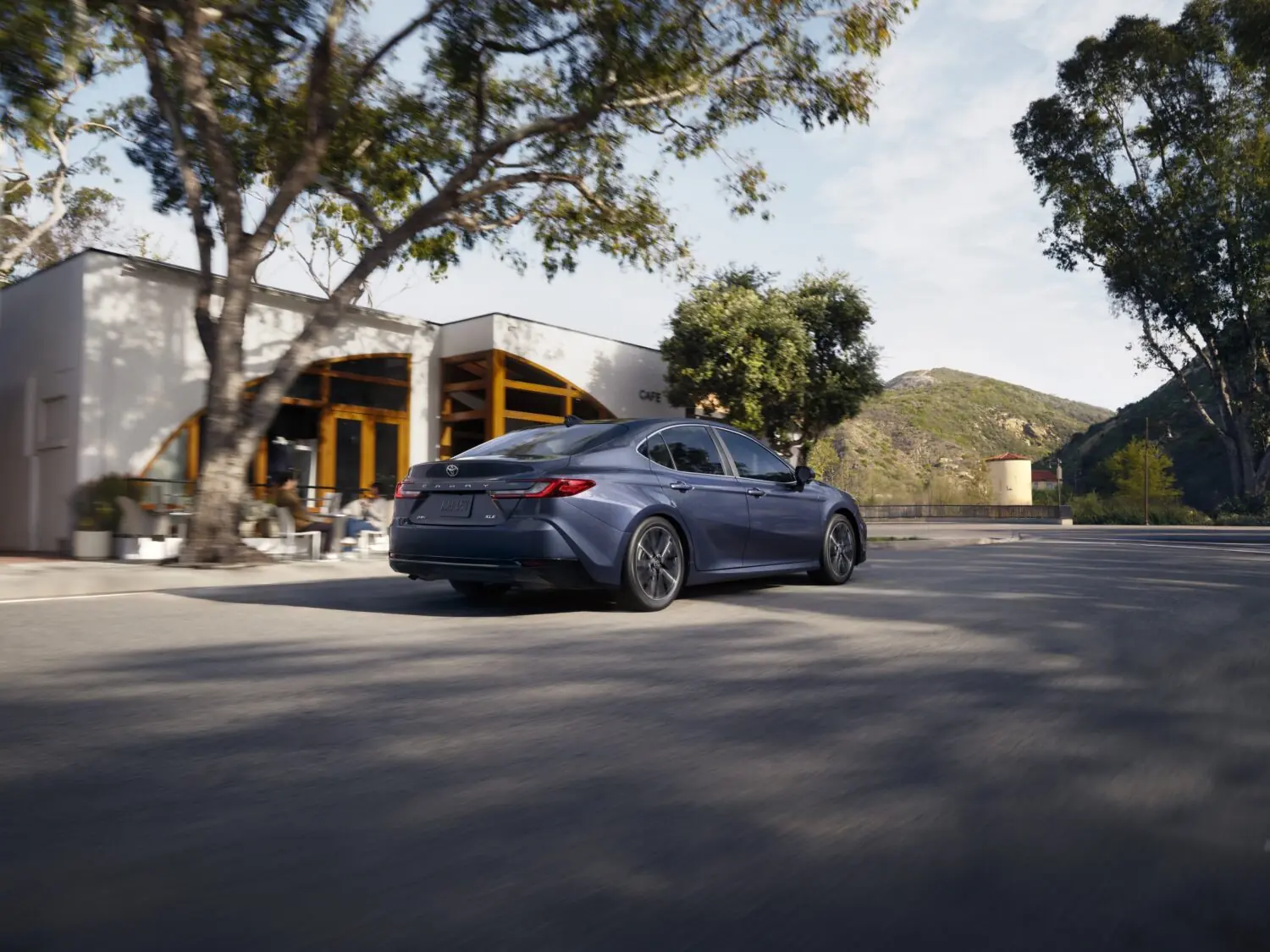 Blue Toyota Camry on a sunny street, rear three-quarter view from the left